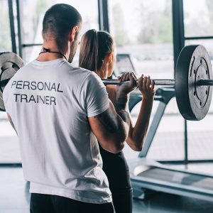 mujer aprendiendo con personal trainer ejercicio de pesa en gimnasio